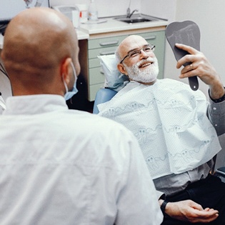 An older man smiling at himself in the mirror while in a dentist chair