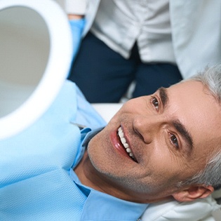 A middle-aged man lying back in a dentist’s chair admiring his new and improved smile thanks to cosmetic dentistry