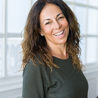 A middle-aged woman wearing a dark gray blouse and smiling after receiving her dental crown