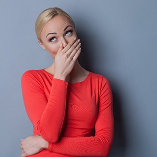 A young woman wearing a red blouse and covering her mouth as she smiles to avoid showing her problem teeth