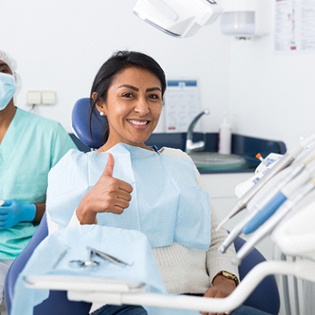 A woman gives a thumbs up while her dentist sits behind her chair in Tappan