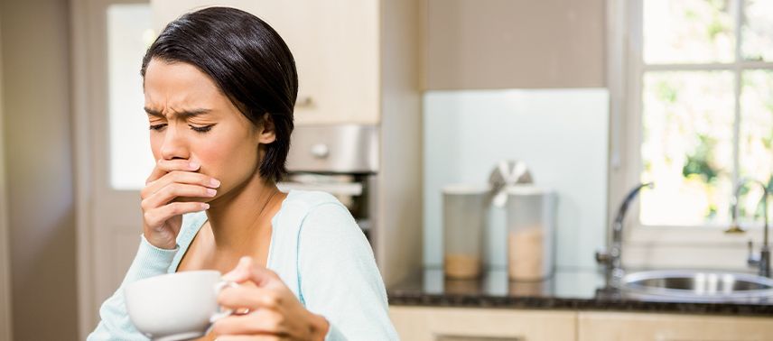 Woman holding coffee cup covering her mouth