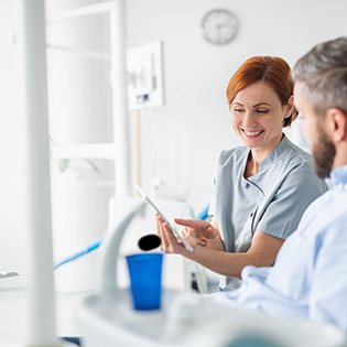 Smiling dental assistant showing patient image on tablet
