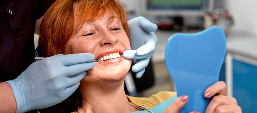 An older woman wearing a yellow blouse and looking at her new smile thanks to dentures in Tappan