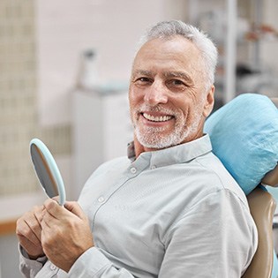 man smiling while holding dental mirror 