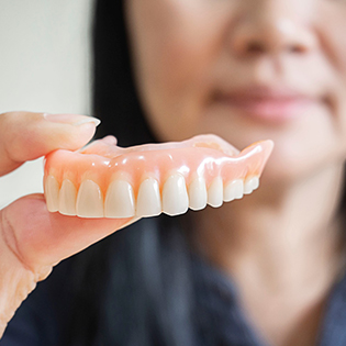 closeup of a woman holding a full denture with her fingers