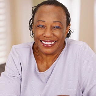 An older woman wearing a lavender blouse smiles while enjoying her whiter, brighter teeth