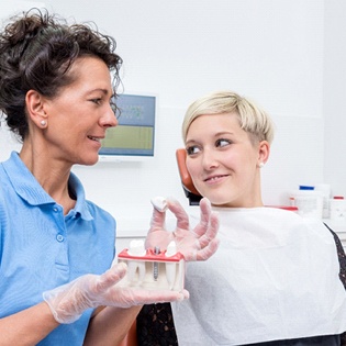 A female patient looking at a dentist who is showing the dental implant parts
