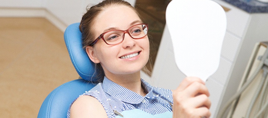 A woman smiling at herself in the dentist chair