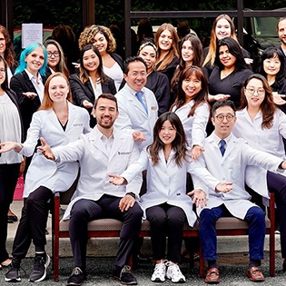 Smile More Dentistry staff smiling and posing enthusiastically in front of a clinic, conveying a welcoming and friendly atmosphere.