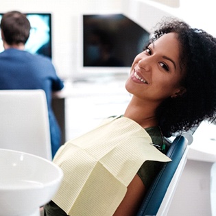 A young woman seated in the dentist’s chair smiling