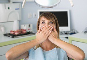 Woman in dental chair covering her mouth