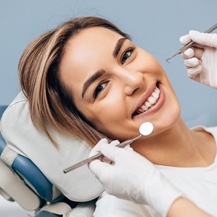 A young female smiling in the dentist’s chair while they check her teeth