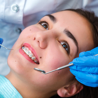 A young woman lying in a dentist’s chair and wearing braces as a dentist prepares to look at her smile