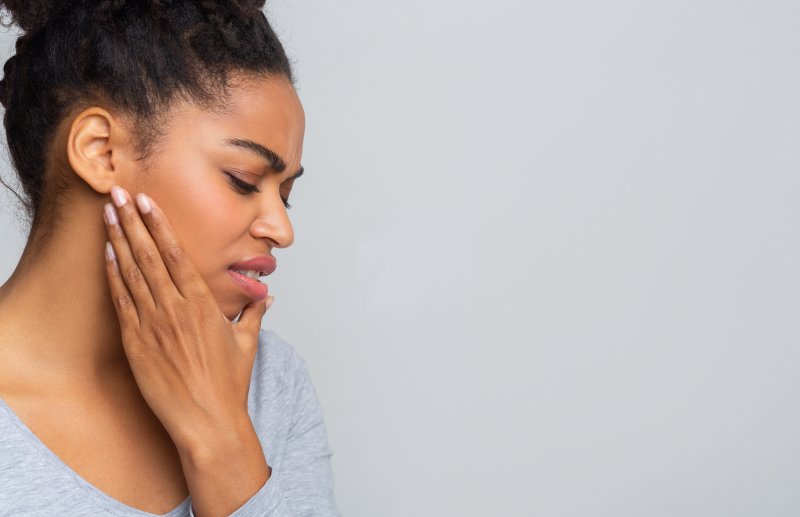 a young woman holding her jaw and cringing in pain as a result of a toothache