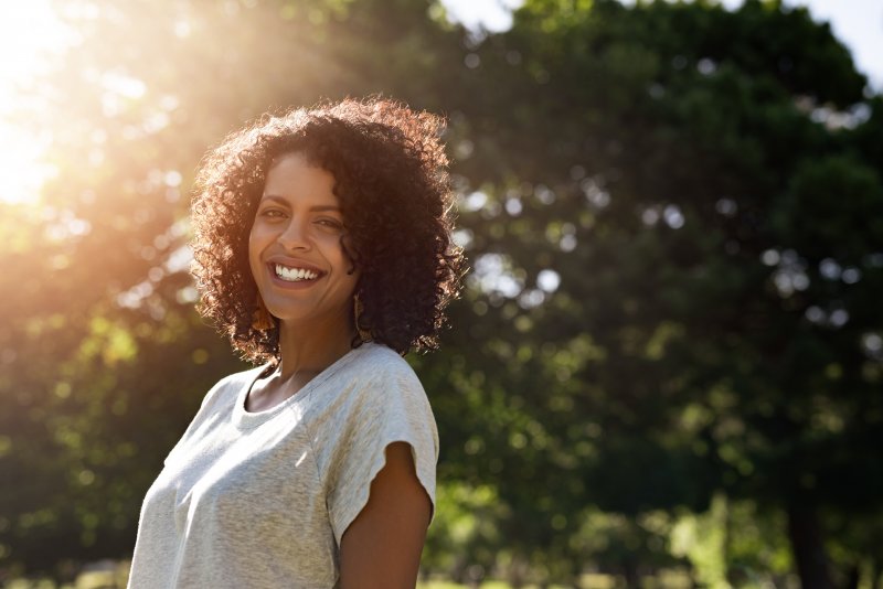 a young woman wearing a gray t-shirt and standing outside, smiling after receiving cosmetic dentistry in Tappan