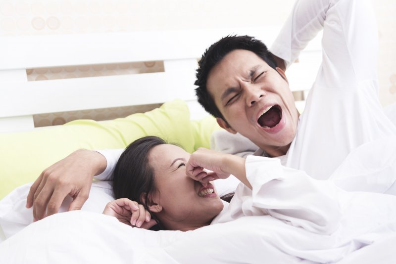 a woman holding her nose while her partner yawns with awful morning breath