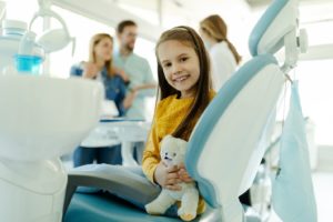 Child smiling while sitting in a chair at the dentist’s office