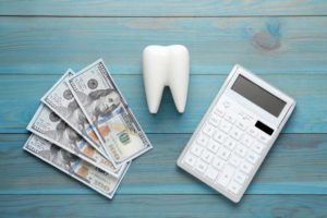 a calculator, large model of a tooth, and money sitting next to each other