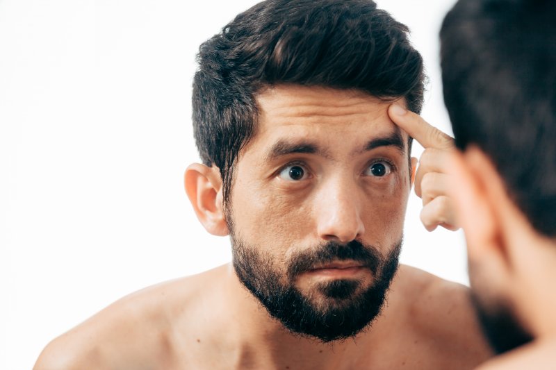 Young man looking in the mirror at his wrinkles