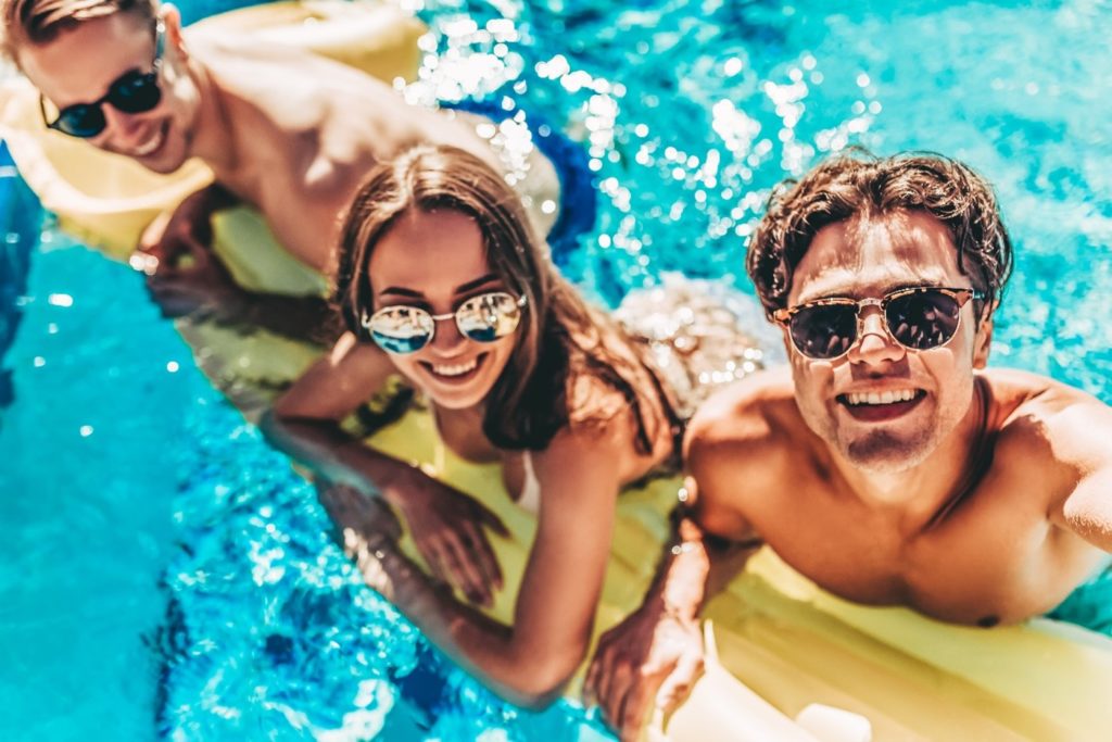 Group of friends smiling while relaxing on noodle in pool