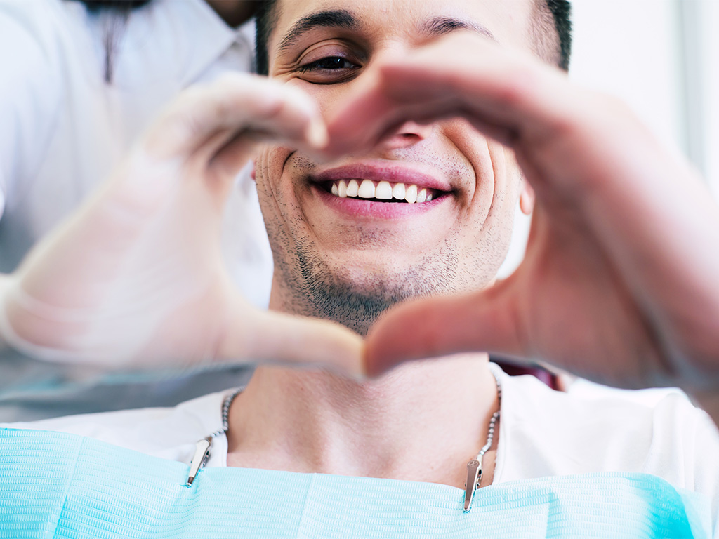A man in dental attire forms a heart shape with his hands, symbolizing care and compassion in dentistry.